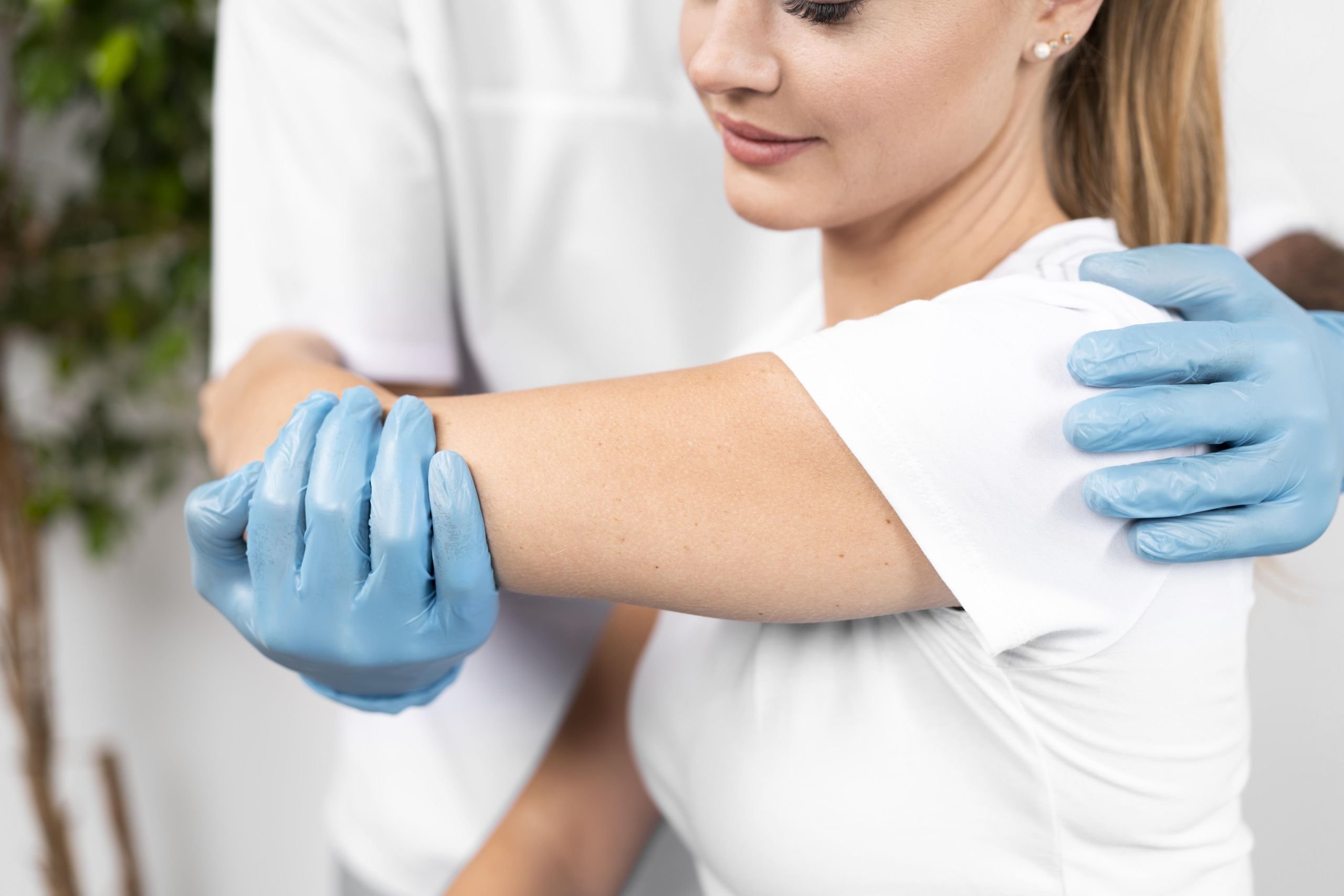 A healthcare professional wearing blue gloves supports and gently manipulates a patient’s arm to assess shoulder joint movement and flexibility.