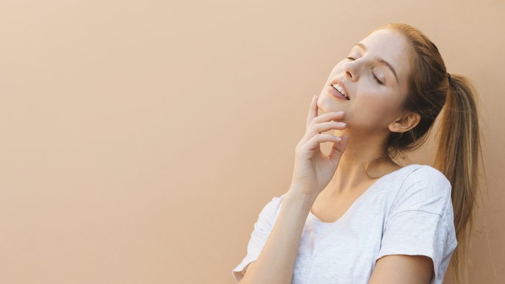 thoughtful-beautiful-young-woman-with-eye-closed-against-beige-backdrop