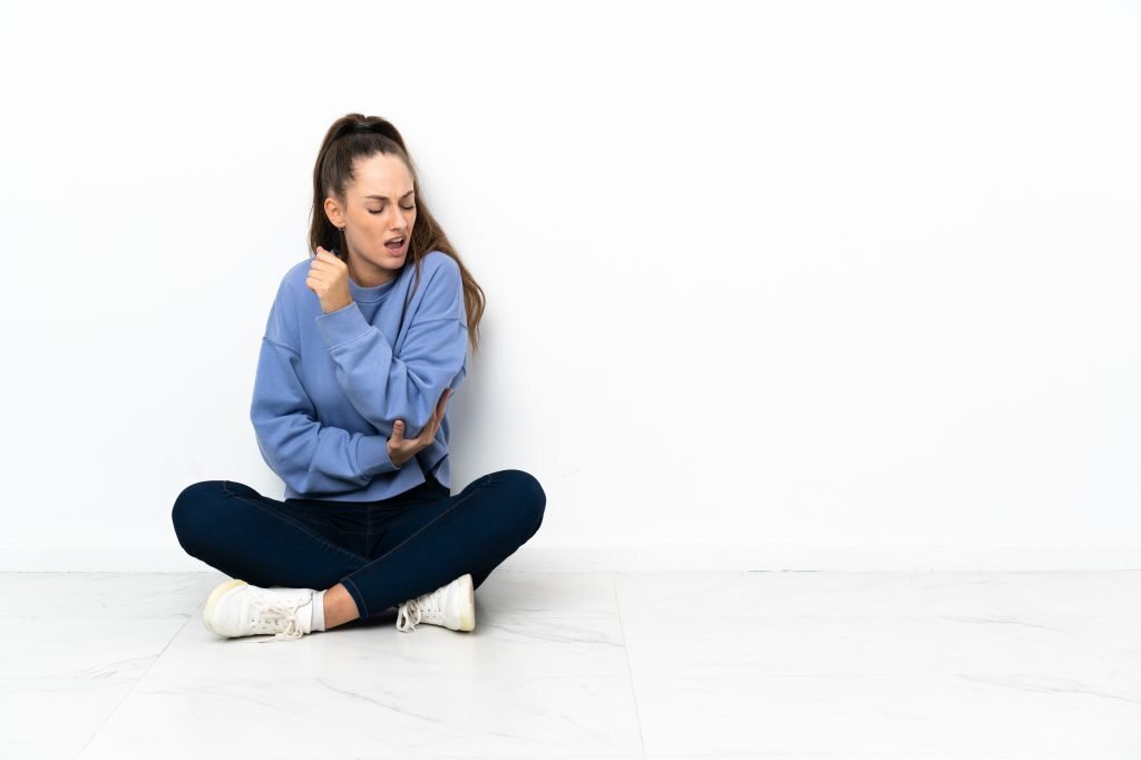 Young woman sitting on the floor with pain in elbow