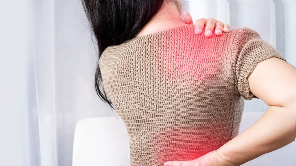 A woman in a beige sweater holding her shoulder and lower back, with a red glow highlighting pain areas.