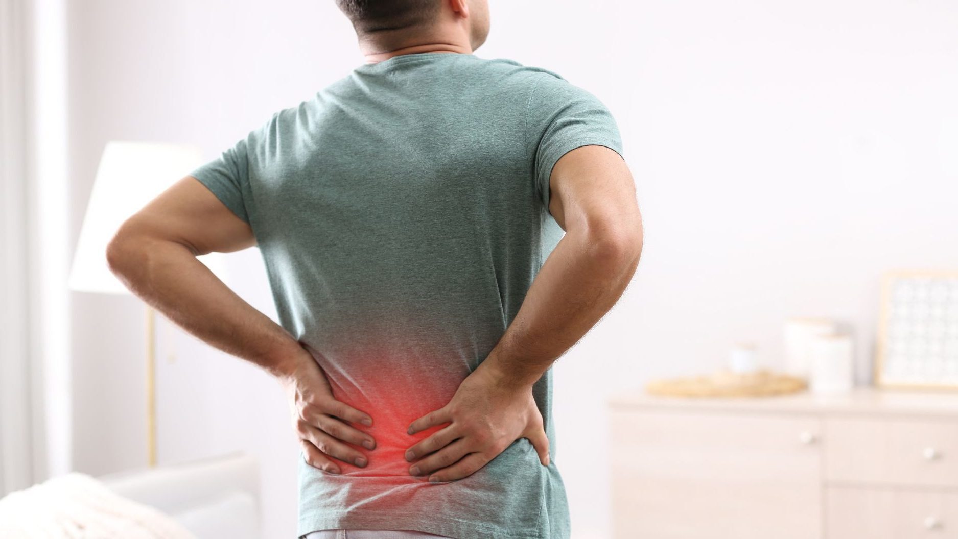 A man in a green t-shirt holding his lower back in pain, with a red glow indicating discomfort.