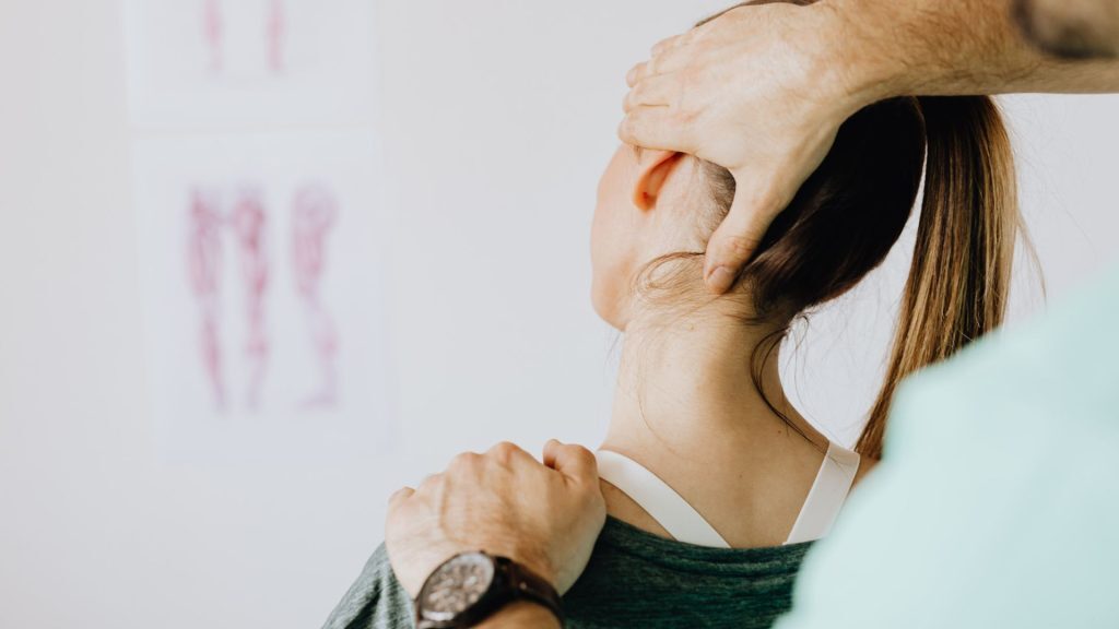 A Chiropractor performing a neck adjustment on a woman with a ponytail in a clinic setting.