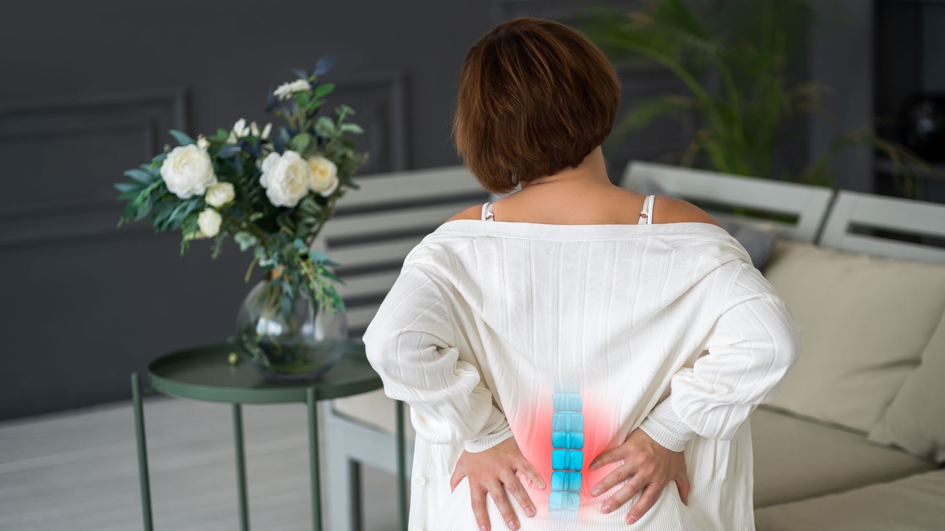 A woman in a white sweater clutching her lower back, with a digitally enhanced spine illustration showing pain.