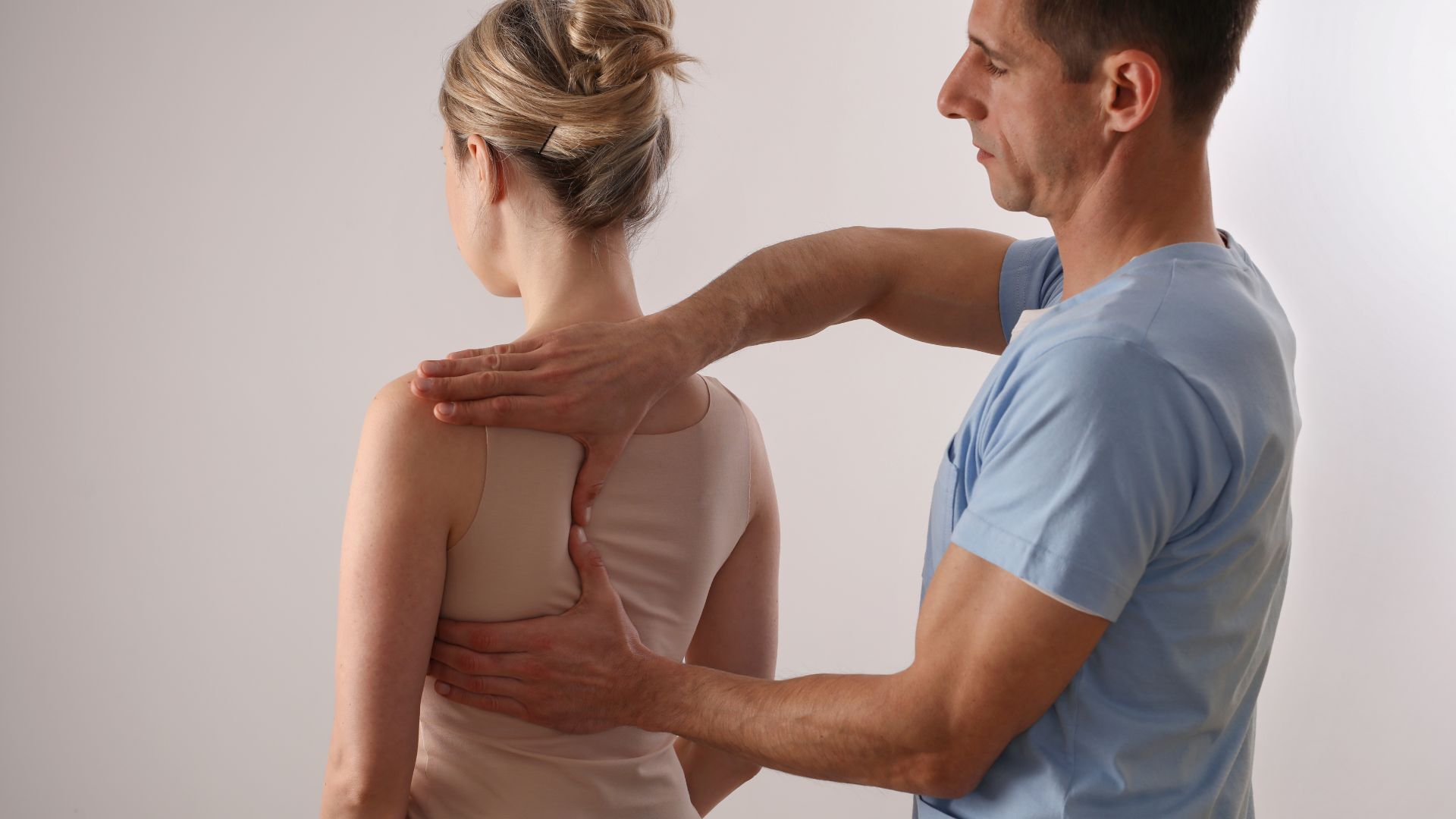 A chiropractor assessing a female patient’s back and spine alignment in a clinical setting.