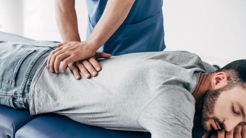 A chiropractor performing a spinal adjustment on a patient lying face down on a treatment table.