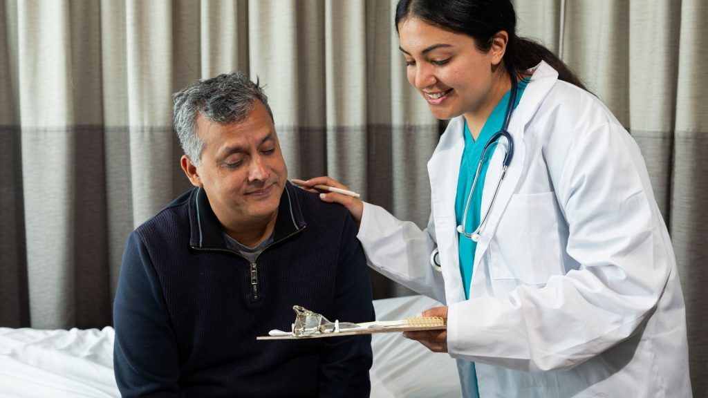 A doctor consulting with a middle-aged male patient, holding a clipboard and providing medical advice.
