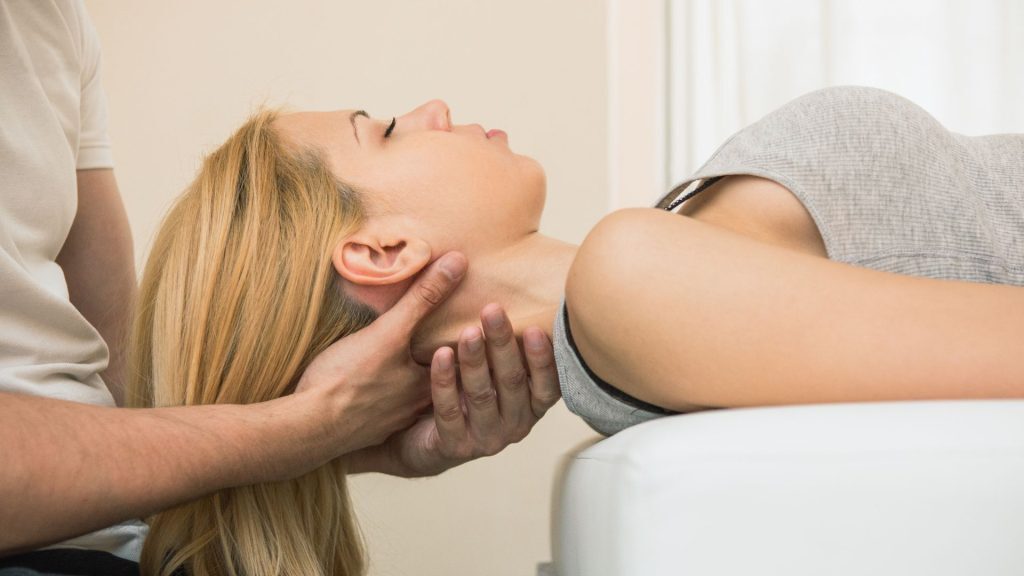A chiropractor performing a neck adjustment on a woman lying on her back during a treatment session.