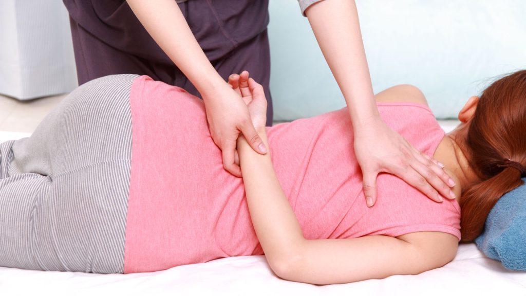 A therapist performing a gentle shoulder and arm adjustment on a woman lying on her side in a relaxed setting.