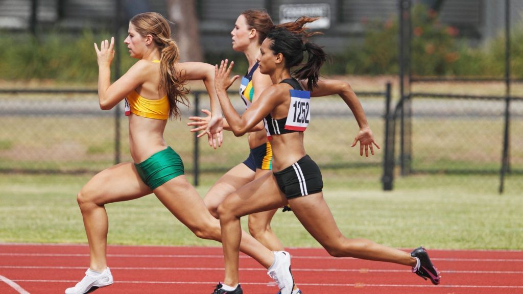 Group of female sprinters in mid-race on an outdoor track, displaying powerful stride and focus.