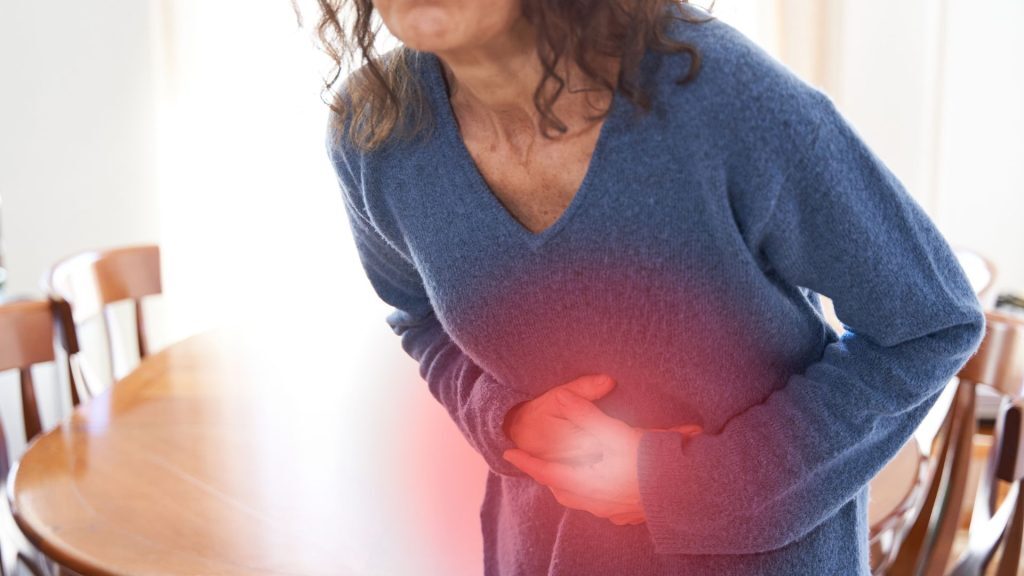 Woman holding her stomach with both hands, showing signs of abdominal pain or digestive issues.
