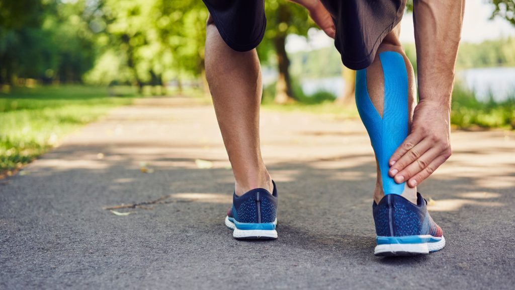 Man outdoors with kinesiology tape on his calf.