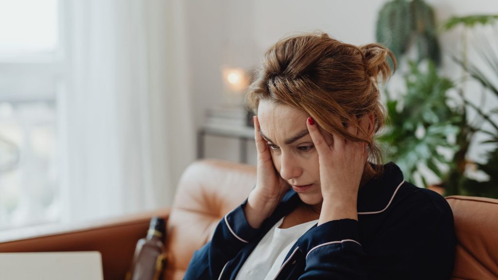 Woman sitting on a couch with her hands on her head, looking stressed.