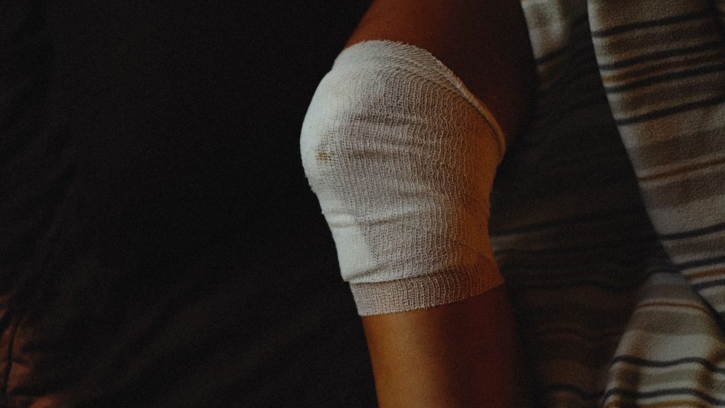 Close-up of a bandaged knee resting on a striped surface.