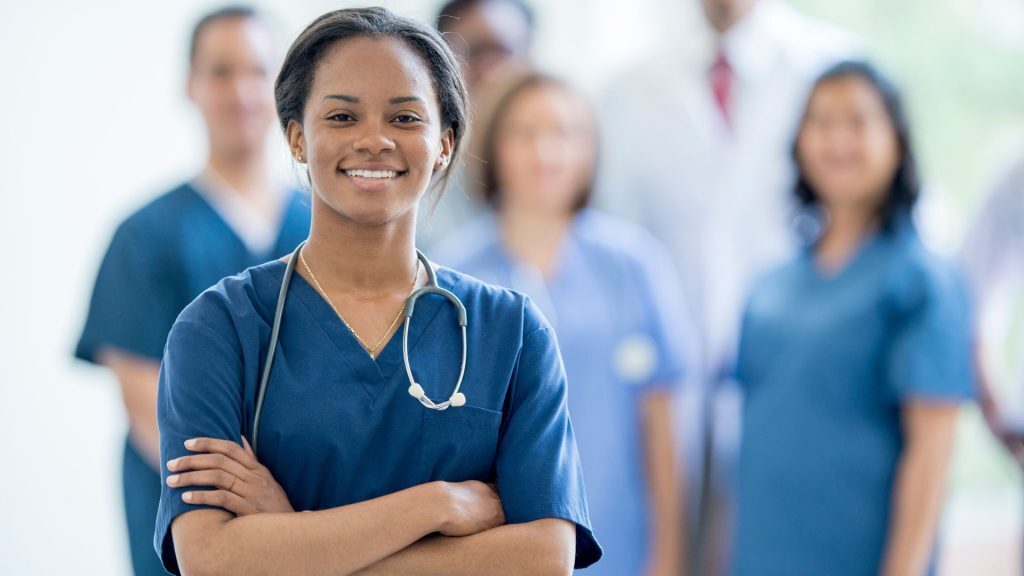 Smiling nurse standing in front of a group of healthcare professionals.