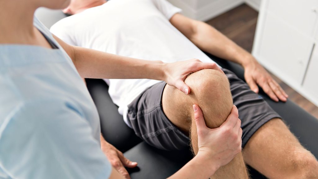 Therapist examining a patient's knee during a physiotherapy session.