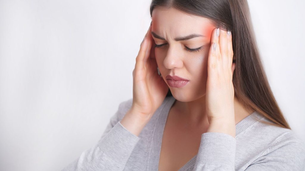 Woman grimacing and touching her temples, with text overlay that reads "Can Physiotherapy Help With Migraines?" indicating headache or migraine pain.
