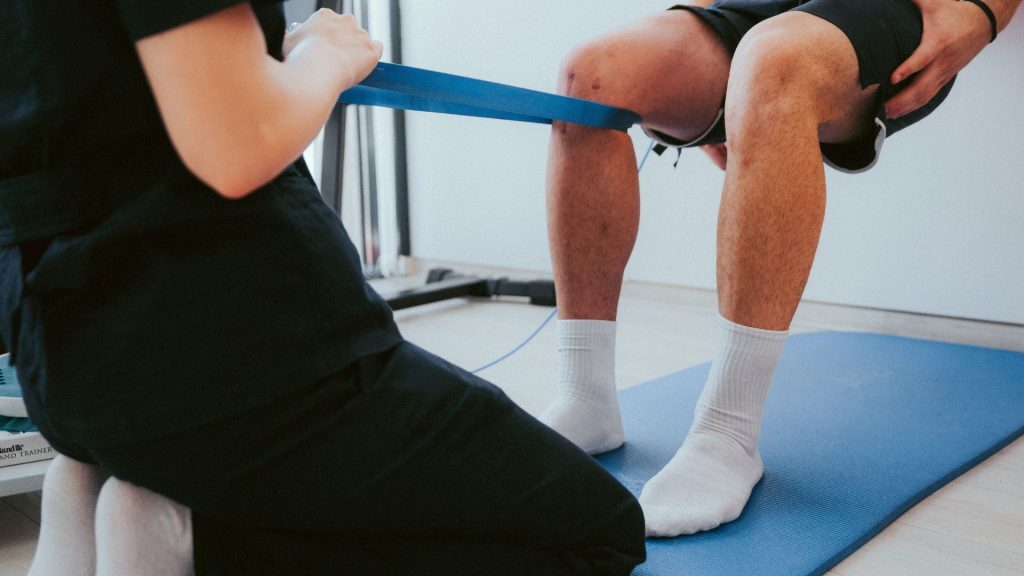 Therapist using a resistance band to assist a man during knee rehabilitation.
