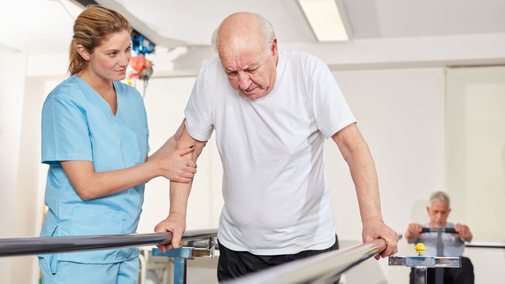 Nurse assisting an elderly man during a walking exercise in a rehab facility.