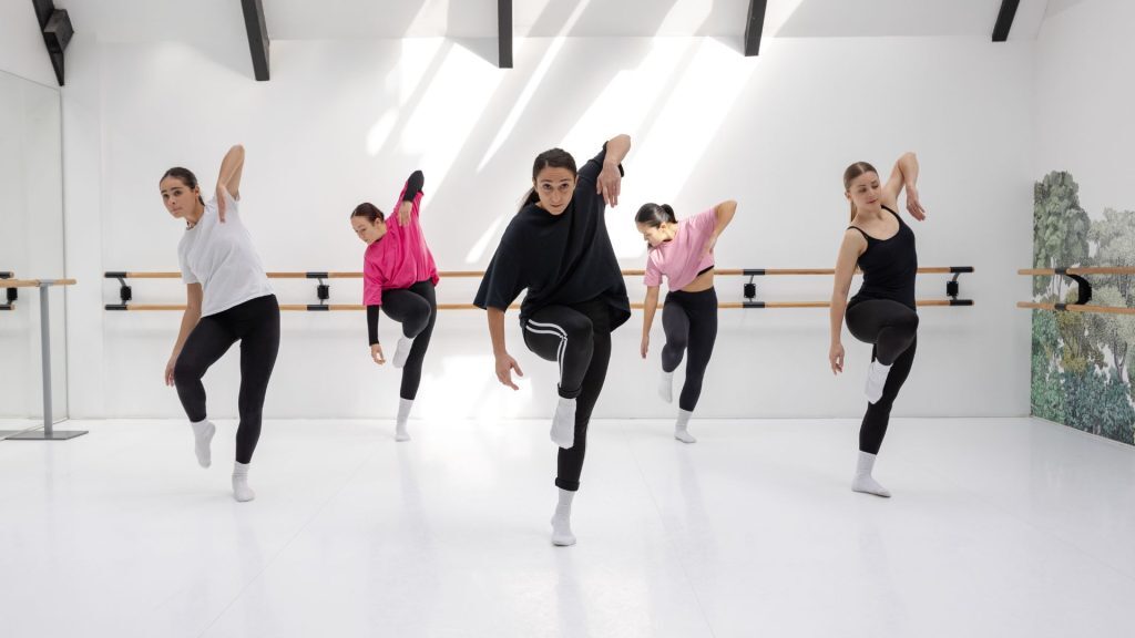 Group of dancers practicing in a bright studio with mirrored walls and barres.